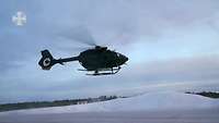 Ein Hubschrauber vom Typ H145M fliegt dich über ein verschneites Gelände