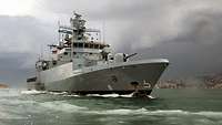 a grey warship swimming in front of a city