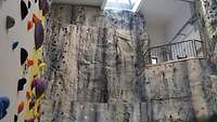 Ein steingraues Felswandimitat mit Haken und eine Boulderwand mit bunten Halte- und Trittgriffen