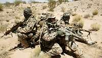 Spezialkräfte bei einer 360° Absicherung in Afghanistan Vier bewaffnete Soldaten hocken im Kreis mit dem Rücken zueinander in der Wüste