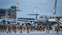 Viele Soldaten laufen über einen Flugplatz vor Flugzeugen vom Typ A400M.