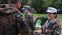 Ein Soldat überreicht einer Soldatin einen silbernen Pokal.
