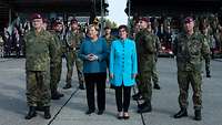 Mehrere Soldaten stehen in Uniform mit zwei zivil gekleideten Frauen vor einer Truppenfahne.