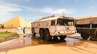 Ein großer weißer LKW der Flughafenfeuerwehr mit UN Schriftzug wird mit Wasser abgespült