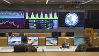 Soldaten sitzen in einem Raum vor Computern und großen Monitoren
