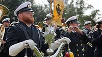 Mehrere Musiker in Marineuniform spielen ihr Instrument.