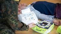 Ein Soldat hält eine Bedienungsanleitung eines Defibrillators in der Hand.