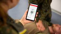 Ein Soldat hält ein Smartphone in der Hand.