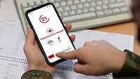 Zwei Hande auf einem Schreibtisch, die ein Smartphone in der Hand halten.