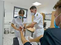 Eingehende Untersuchung Eine Soldatin und ein Soldat in weißer Arztkleidung begutachten den Fuß eines Patienten, der auf einer Liege sitzt.