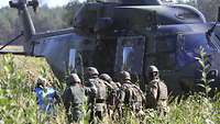 Eine Rettungssanitäterin und fünf Soldaten fassen sich hintereinander an der Schulter und laufen auf einen Hubschrauber zu. 