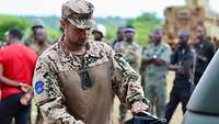 Ein deutscher Soldat steht vor malischen Soldaten und gießt sich Kaffee aus einer Thermoskanne ein