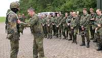 Ein Soldat kontrolliert das angelegte Gurtzeug eines Jugendlichen, mehrere Jugendliche stehen im Halbkreis drum herum.