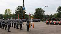 Auf einem gepflasterten Platz stehen am Rand in Formationen zahlreiche Soldaten in Dienstanzügen.