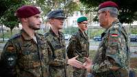 Drei Soldaten stehen nebeneinander. Ein vierter steht ihnen gegenüber und überreicht dem mittleren Soldaten eine Ehrenmünze.