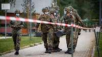 Eine Gruppe Soldaten trägt gemeinsam einen schweren, dunklen Metallgegenstand. 