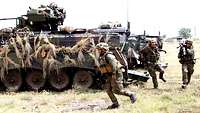 Soldaten stürmen aus einem Panzer.