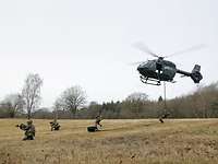 Vier Soldaten seilen sich aus einem Hubschrauber ab und nehmen Stellung auf einer Wiese ein