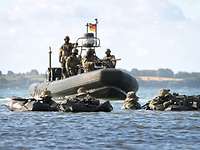 Bewaffnete Kampfschwimmer in Stellung im Wasser, ein Schlauchboot mit Soldaten dahinter