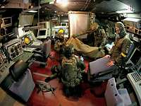 Soldaten in der Operationszentrale unter Deck eines Schiffes hocken und stehen um einen am Boden liegenden Verwundeten