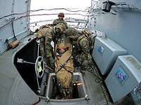 Soldaten transportieren einen Verwundeten auf einer Trage durch eine Luke vom Unterdeck ans Oberdeck eines Schiffes