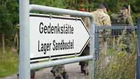 Soldaten gehen hinter einem Hinweisschild vorbei.