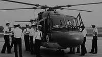 Mehrere Menschen in Uniform besichtigen einen Hubschrauber.