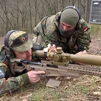 Ein liegender Soldat mit einem Scharfschützengewehr im Anschlag, eine anderer Soldat knient daneben