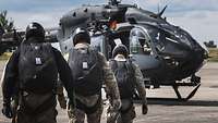 Fallschirmsprung KSK Soldaten mit Helmen und Fallschirmrucksäcken laufen zu einem Hubschrauber vom Typ H145M