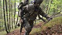 Ein Soldat steigt im Wald an einem Seil gesichert einen Berg hinauf.