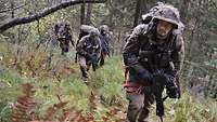 Soldaten gehen mit viel Gepäck einen steilen Hang im Wald hinauf.