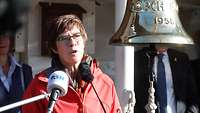 Einlaufen „Gorch Fock“ AKK Eine Frau in roter Jacke spricht in unterschiedliche Mikrofone.