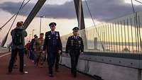Zwei Generäle gehen eine Brücke entlang. Ihnen folgen mehrere Soldaten.