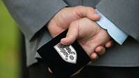 Ein Soldat hält hinter seinem Rücken eine kleine schwarze Schatulle mit einer Metallplakette fest. 
