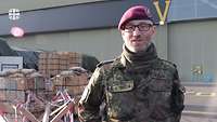 Ein Soldat in Uniform steht sprechend vor einer Kamera.
