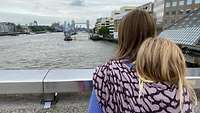 Eine Mutter und ihr Kind stehen auf einer Brücke und schauen auf die Themse in London.