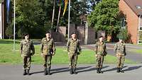 Fünf Soldaten sind auf einer Straße in der Kaserne nebeneinander angetreten.
