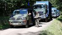Mehrere Bundeswehrkraftfahrzeuge stehen in einem Wald auf einer Straße. 