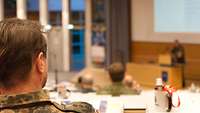 Ein Soldat sitzt im Hörsaal und schaut zur Bühne.