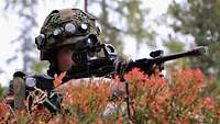 Ein Soldat in Gefechtsanzug liegt mit seinem Maschinengewehr auf herbstlich rotem Waldboden.
