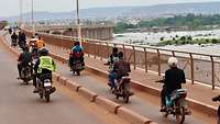 Einige Motorräder überqueren auf einer Brücke einen breiten Fluss