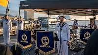 Eine Marinesoldatin in weißer Uniform steht hinter einem Mikrofon und singt.
