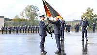 Zwei Soldaten in blauen Uniformen stehen sich gegenüber. Der eine überreicht dem anderen eine Deutschland-Flagge.
