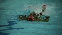 Soldat schwimmt in Uniform auf dem Rücken.