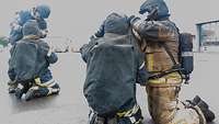 Personen mit Feuerschutzausrüstung helfen sich gegenseitig, diese abzulegen.