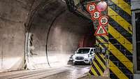 Fahrzeug kommt aus einem Tunnel, auf dessen Seitenwand von außen mehrere Verkehrsschilder prangen.