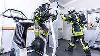 Übung Feuerwehr Ergometer und Hammerzug Ein Feuerwehrmann in voller Ausrüstung auf einem Fahrradergometer, ein weiterer zieht an einem Hammerzug.