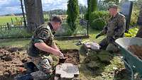 Zwei Soldaten legen einen Grabstein frei