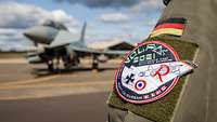 Auf einer Fliegerkombi klebt ein Patch mit dem Wppen von VOLFA, im Hintergrund ein Eurofighter.