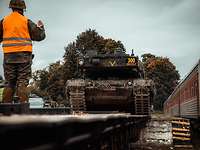 Ein Kampfpanzer fährt auf einen Eisenbahnwaggon. Auf dem Wagon steht ein Soldat und weist den Kraftfahrer ein
